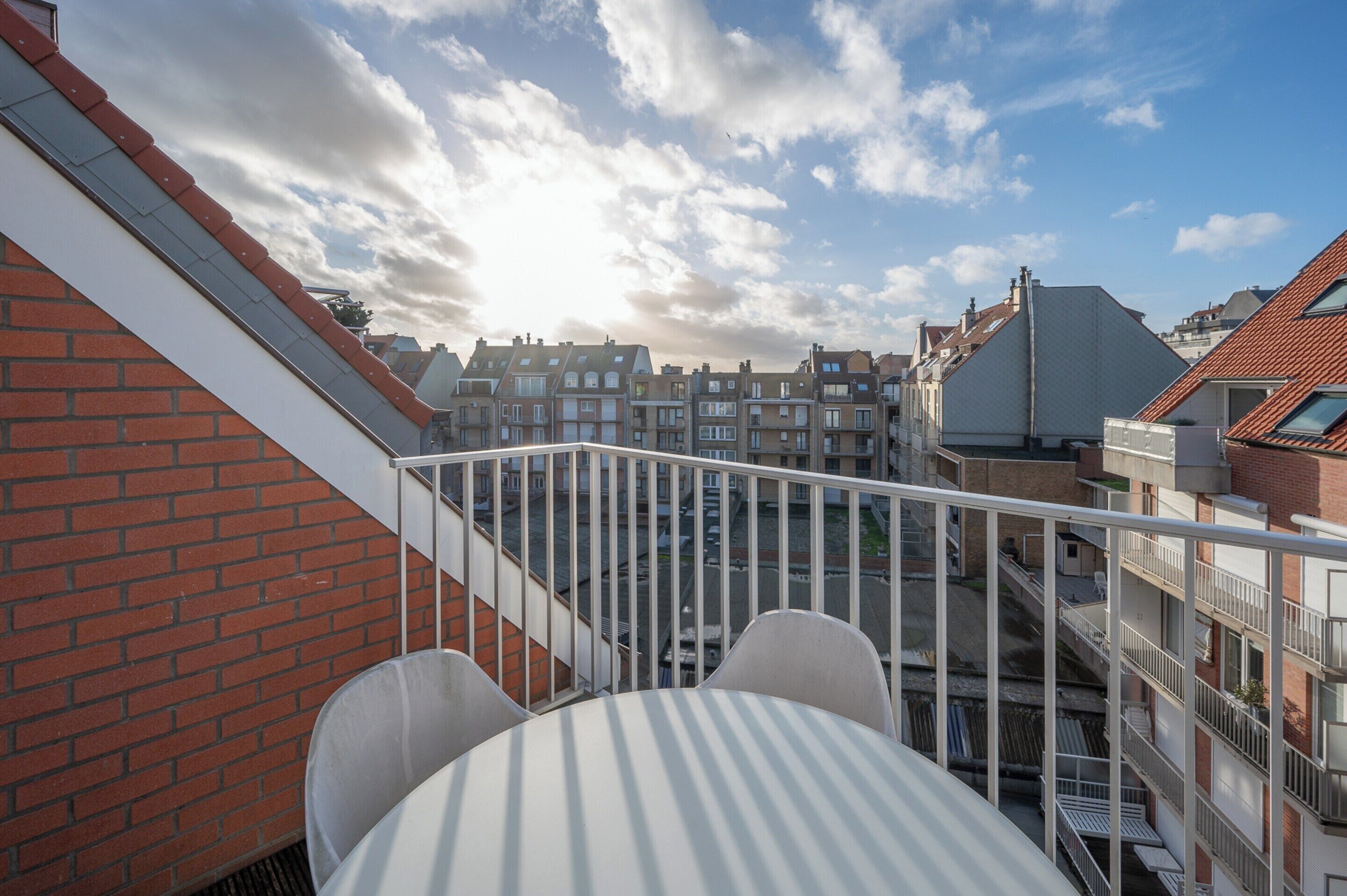 A balcony with a white railing, a brick wall, and a view of neighboring buildings.