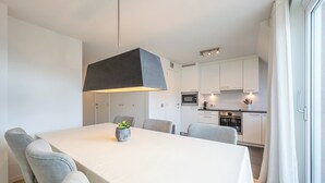 A modern kitchen with white cabinets, a central island, and a dining area with a table and chairs. - Apartment on Belgian Coast Near Beaches (Knokke-Heist)