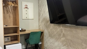 A compact room with a built-in desk, a TV mounted on the wall, a small fridge, and a wooden wardrobe with hanging clothes. - HOTEL BAHIA AZUL  (Cartagena)