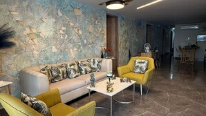 A modern living room with a sofa, two yellow chairs, a coffee table, a ceiling fan, and a textured wall. - HOTEL BAHIA AZUL  (Cartagena)