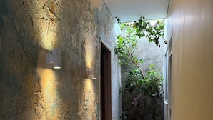 Un couloir aux murs texturés, doté d’un sol carrelé et d’une porte donnant sur une pièce offrant une vue sur la verdure.