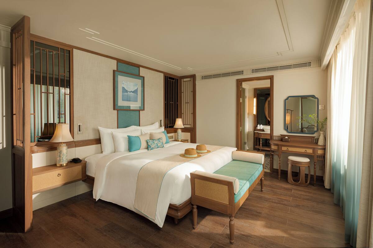 A hotel room with a large bed, bedside tables, a desk, a chair, a mirror, and a window with curtains.