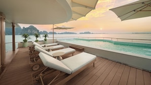 A deck with sun loungers and a pool, overlooking a body of water and distant mountains. - Bhaya Soul - Wellness Inclusive Cruise (Tuan Chau)