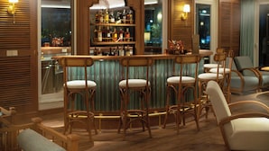 A bar area with wooden bar stools, a bar counter, and a shelf of bottles. - Bhaya Soul - Wellness Inclusive Cruise (Tuan Chau)