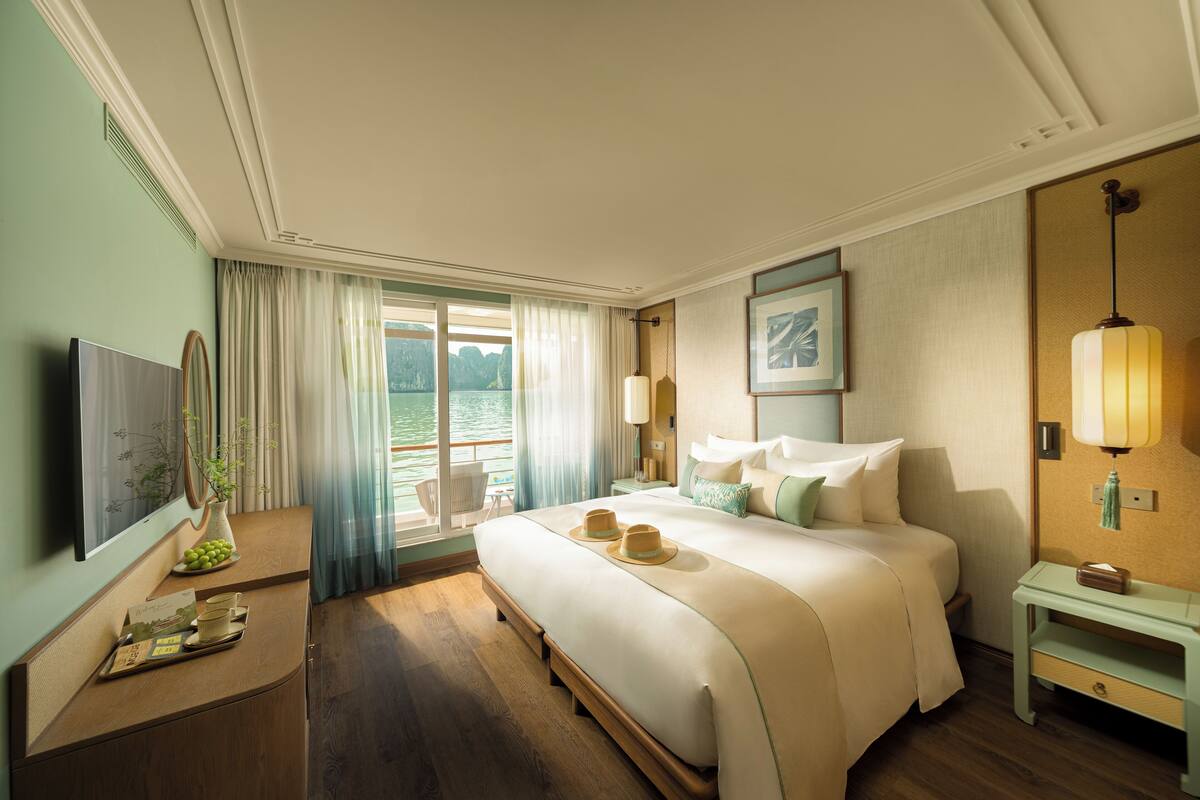 A hotel room with a large bed, a television, a desk with a lamp, and a view of the outdoors.
