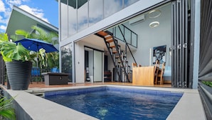 A modern house with a swimming pool, a wooden deck, and a staircase leading to the upper floor.