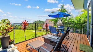 A wooden deck with a pool, lounge chairs, a table, and a blue umbrella.