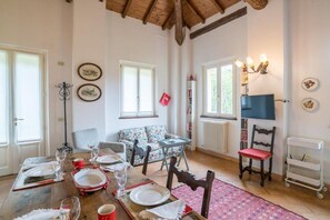 A dining area with a wooden table set for four, a sofa, a TV, and a radiator.