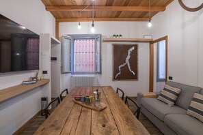 Spiseområde med et træbord, stole, en sofa, et fjernsyn og et vindue med tremmer.