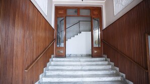 Una escalera de mármol que conduce a una puerta de madera con paneles de vidrio y una barandilla metálica.