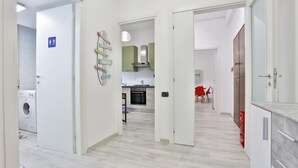 Una cocina moderna con armarios blancos, un comedor con una silla roja y una lavadora a la vista.