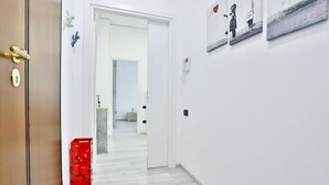 Un pasillo con una puerta de madera, un caja roja y una pared blanca con un cuadro enmarcado.
