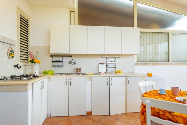 A compact kitchen with white cabinets, a gas stove, a sink, and a window with blinds.