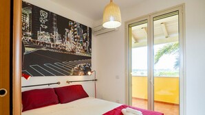 A hotel room with a bed, a red bedspread, a poster of a cityscape, a ceiling light, and a sliding glass door to a balcony. - GuestHost - Villa Mirò - Escape to Salento (Melendugno)