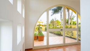 A room with a large arched glass door leading to an outdoor area with potted plants and a yellow wall. - GuestHost - Villa Mirò - Escape to Salento (Melendugno)