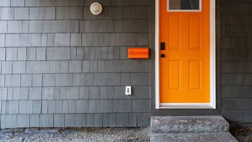 A house with a gray shingled exterior, a bright orange door, a small mailbox, and a step leading to the door.
