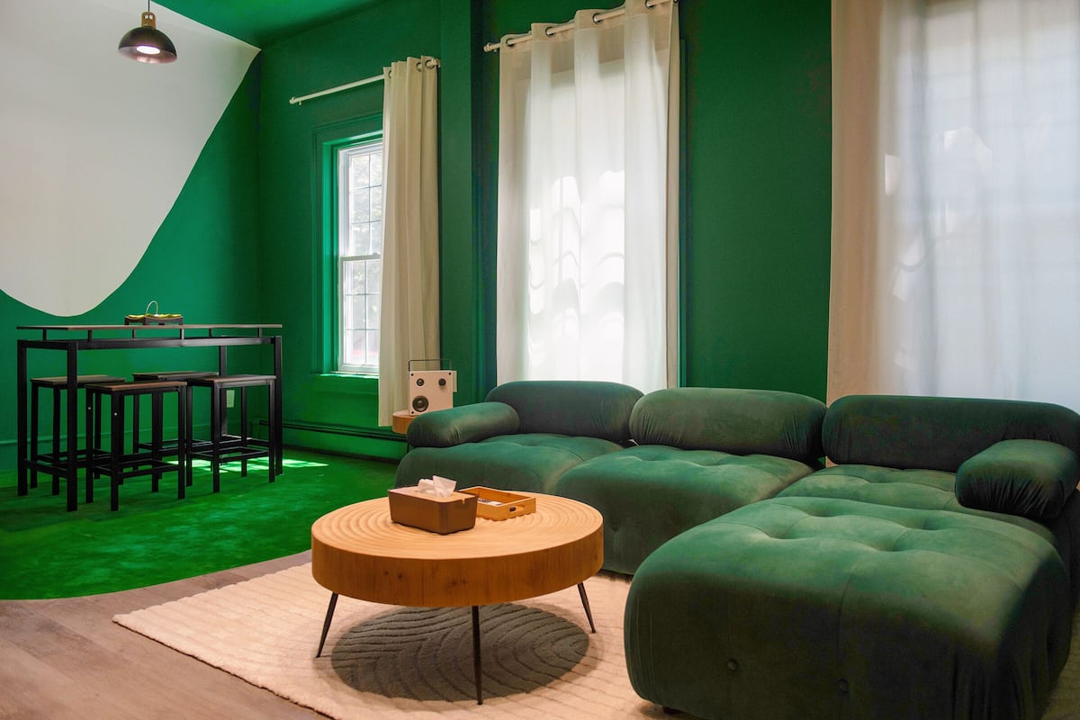 Een woonkamer in groene tinten met een hoekbank, een ronde houten salontafel en een klein tafeltje met krukjes.