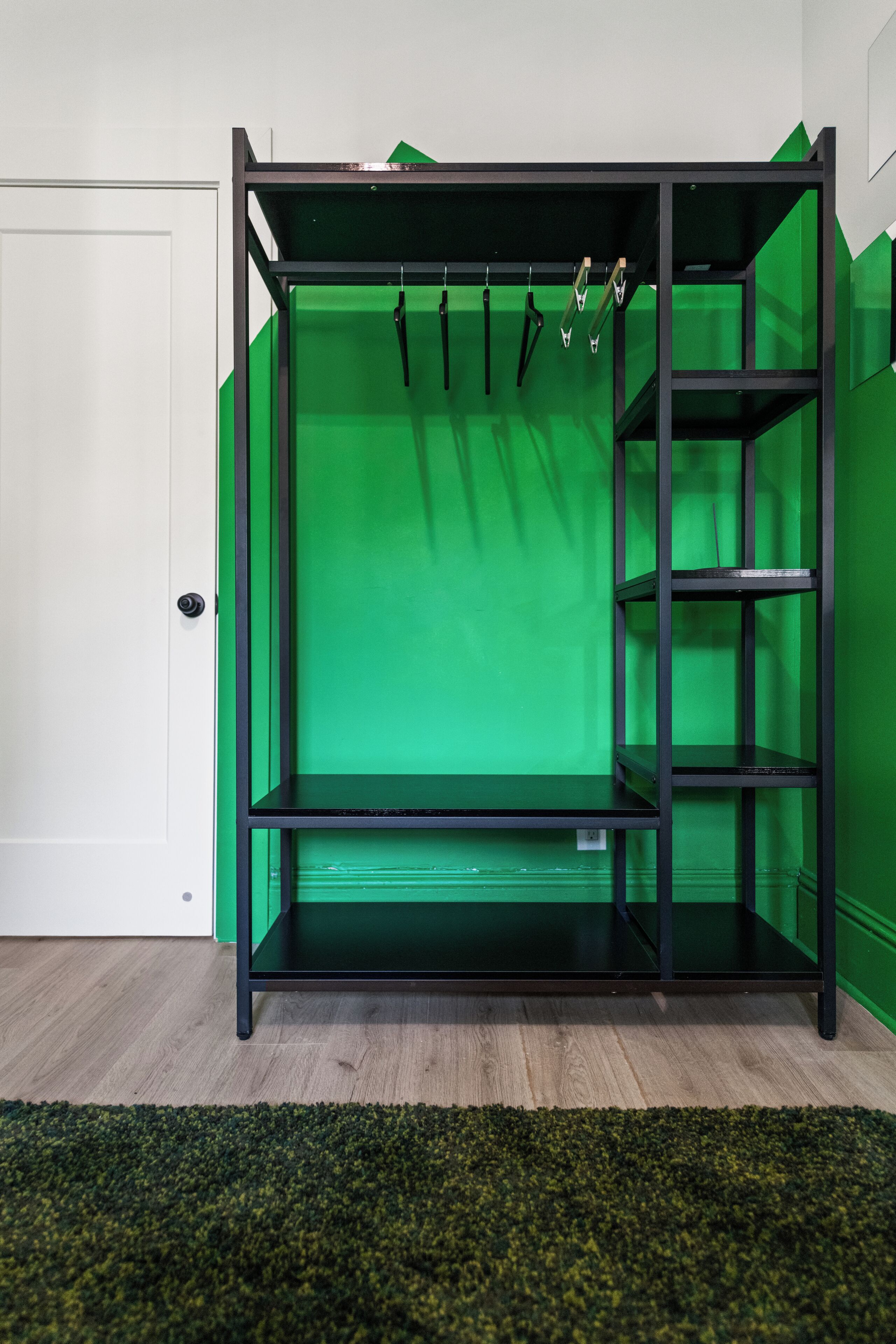 A room with a green screen, black metal shelving, and a white door.