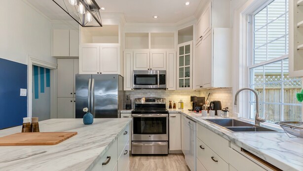A modern kitchen with white cabinets, stainless steel appliances, a marble countertop, and a window providing natural light. - Downtown Sustainable Garden House (Halifax)