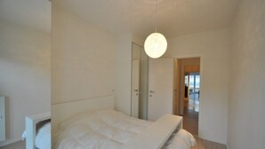 A modern bedroom with a large bed, a walk-in closet, and a hallway leading to another room. - Modern 5th Floor Apartment (Knokke-Heist)