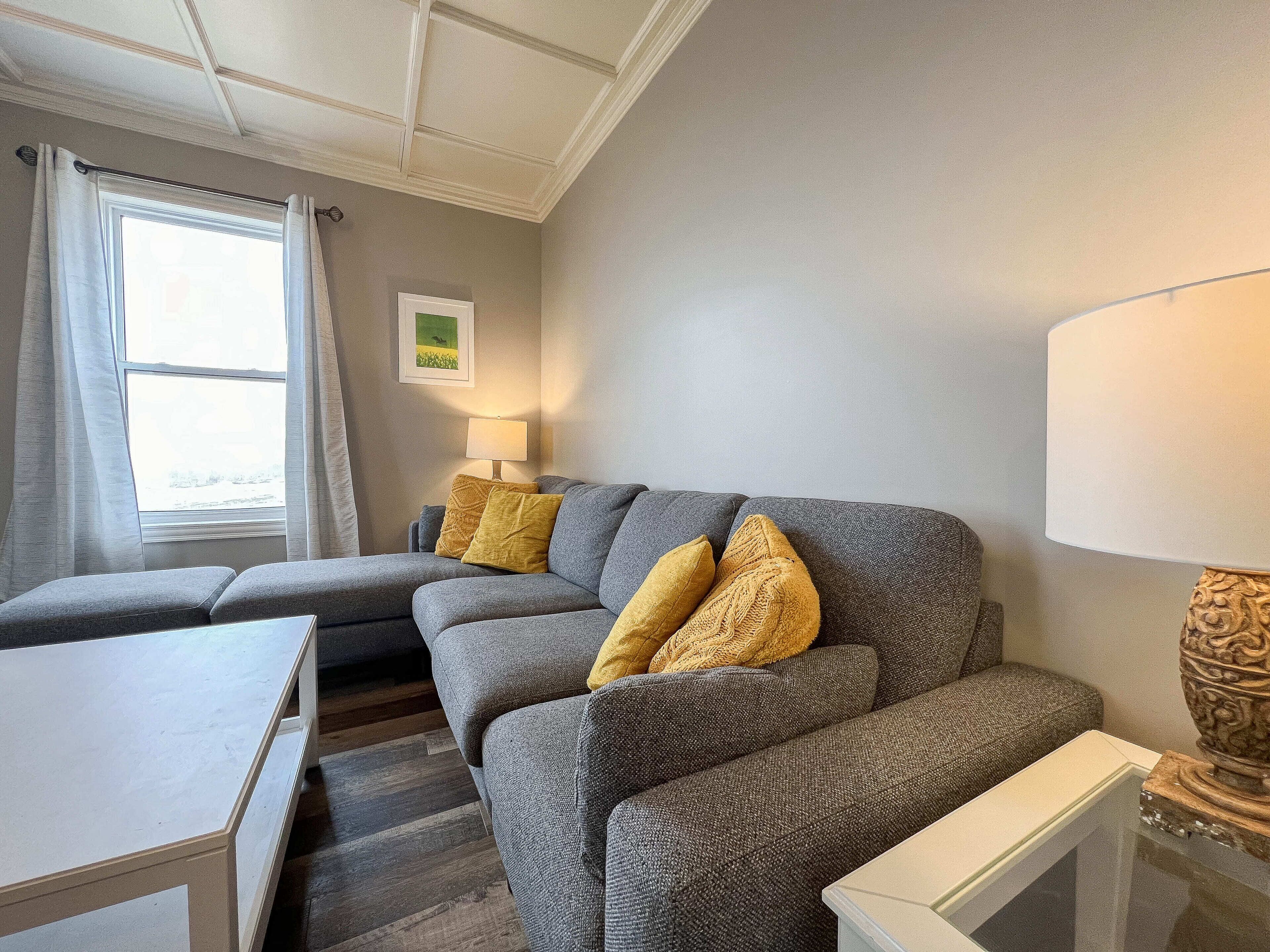 A modern living room with a grey sofa, a small table, and a lamp.