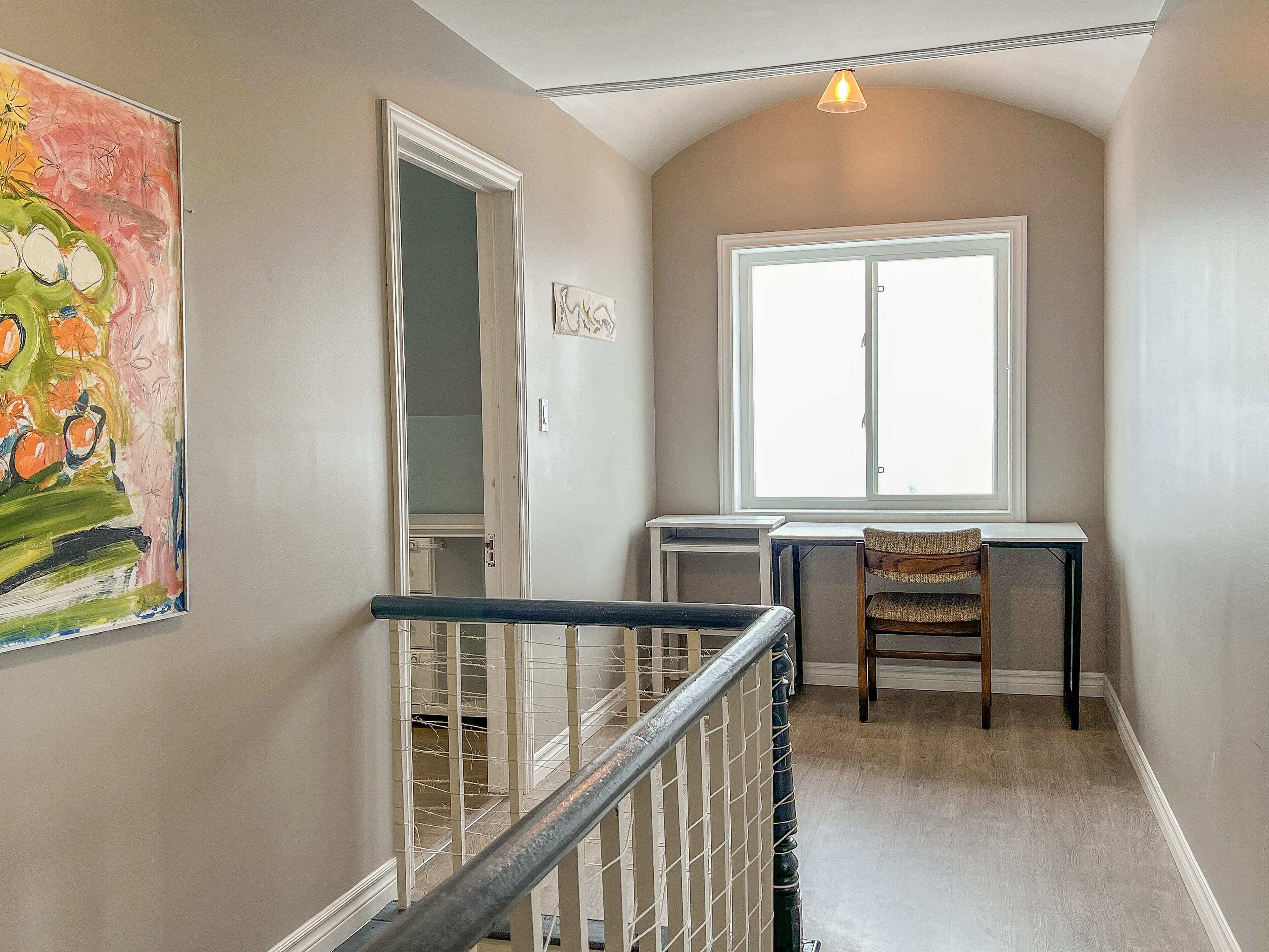 Un couloir avec un escalier, un bureau avec une chaise et une grande fenêtre.