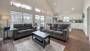 A spacious living room with two grey sofas, a coffee table, and a large window overlooking a deck.