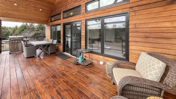 A covered patio with wooden flooring, a grill, wicker furniture, and large sliding glass doors.