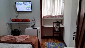 A small, cozy room with a bed, a desk, a chair, and a television. - Azure Flats (Curitiba)