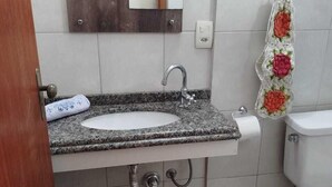 A bathroom with a granite sink, a wooden-framed mirror, a toilet, and a shower curtain with floral patterns. - Azure Flats (Curitiba)