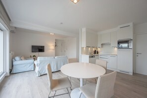 Un appartement moderne et bien éclairé, comprenant un coin repas, une kitchenette et un espace de vie.
