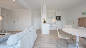 A modern kitchen with white cabinets, a central island, and a dining area with a white table and chairs.