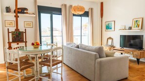 Sala de estar com sofá, televisão, escrivaninha de madeira e um espaço de jantar com cadeiras e mesa.