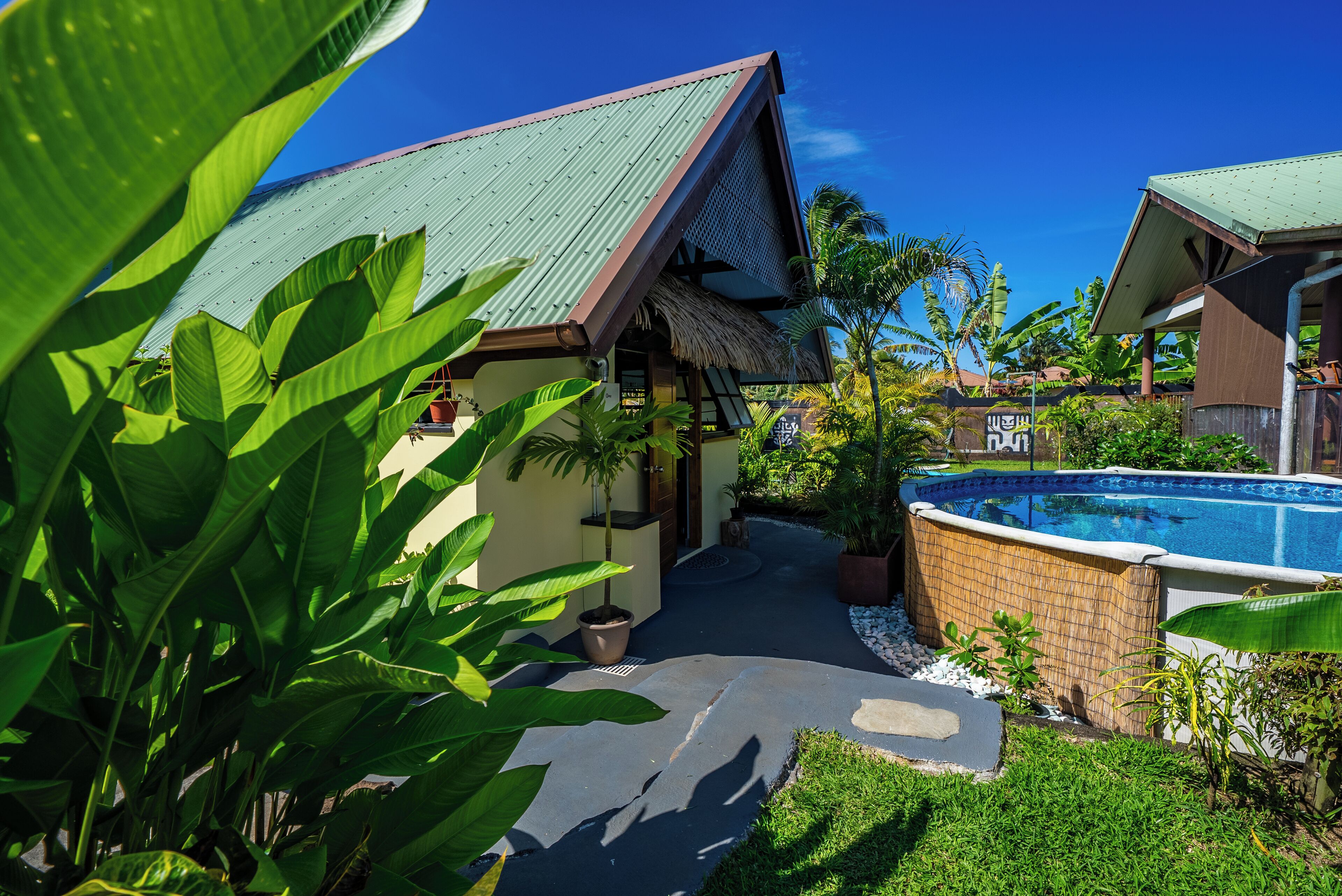 A house with a green roof, a swimming pool, and lush greenery.