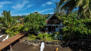 A house with a wooden deck and a small dock extending into a body of water. - Toahere Beach House - Beachfront - Pool - Pontoon (Papeari)