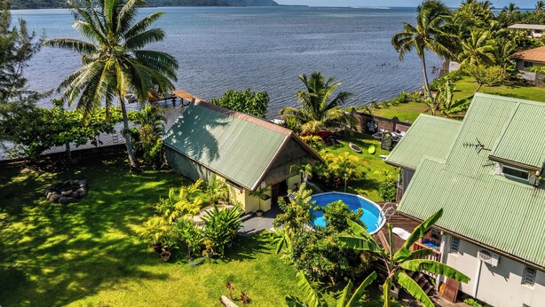 A tropical resort with a swimming pool, lush greenery, and a view of the ocean and mountains. - Toahere Beach House - Beachfront - Pool - Pontoon (Papeari)