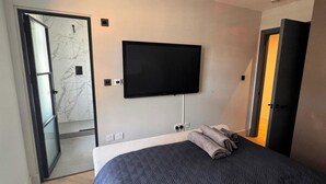 Habitación de hotel moderna con una cama grande, un televisor de pantalla plana montado en la pared y una puerta que da a un baño.