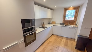 Una cocina moderna con armarios blancos, horno integrado, microondas y ventana con vistas a un paisaje nevado.