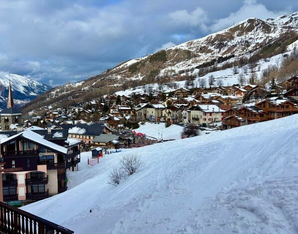 Un pueblo cubierto de nieve con casas de madera tradicionales, una iglesia y montañas al fondo.