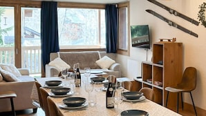 Un comedor con una mesa larga dispuesta para cuatro personas, un sofá y un televisor montado en la pared.