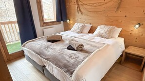 Un dormitorio de cabaña de madera con una cama, dos almohadas, una mesita de noche y una ventana con cortinas.