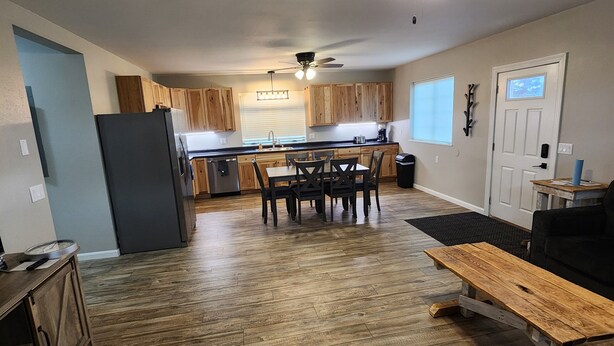 A spacious kitchen with wooden cabinets, a dining table with chairs, a ceiling fan, and a black refrigerator.