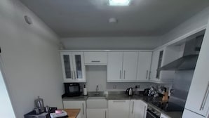 A modern kitchen with white cabinets, a wooden countertop, and a stainless steel range hood. - Modern Apartment - Quiet Location (Doncaster)