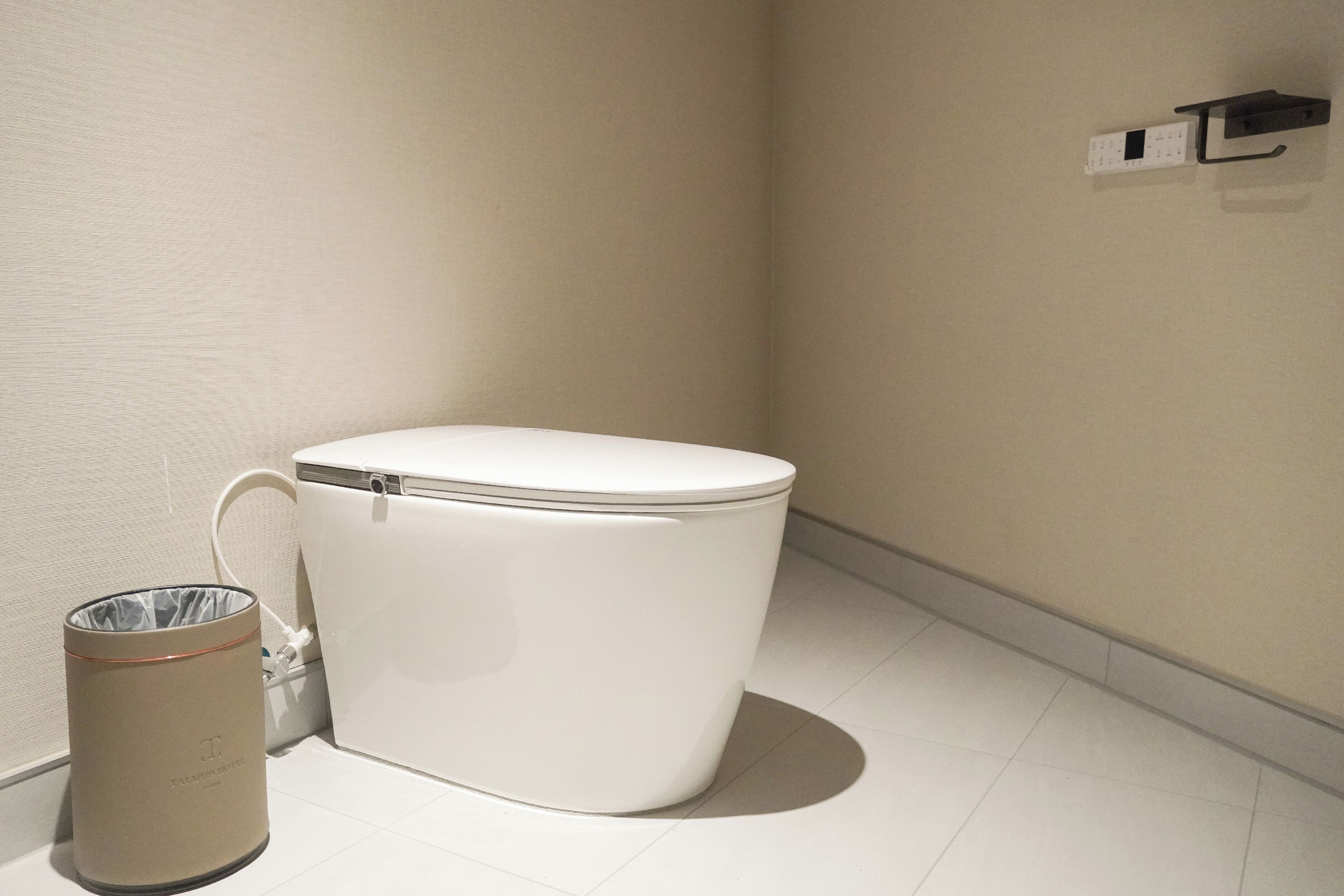 A white toilet with a lid, a trash can, and a wall-mounted electrical outlet.