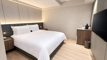 A modern hotel room with a large bed, bedside tables, a TV, and a small kitchenette.
