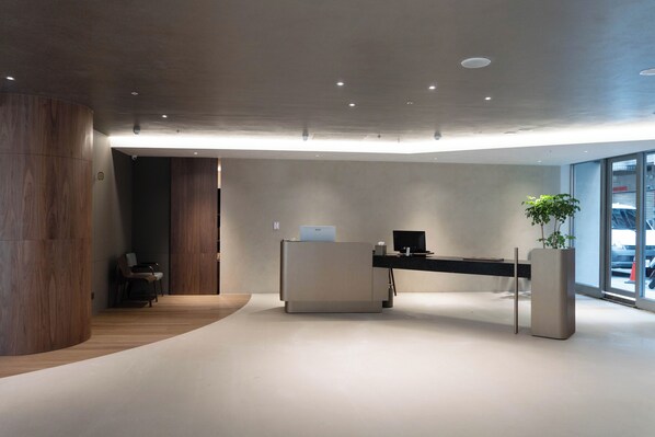 A modern reception area with a wooden column, a reception desk, and a potted plant. - TALMUD HOTEL CLASSIC TAIWAN BOULEVARD (Taichung)