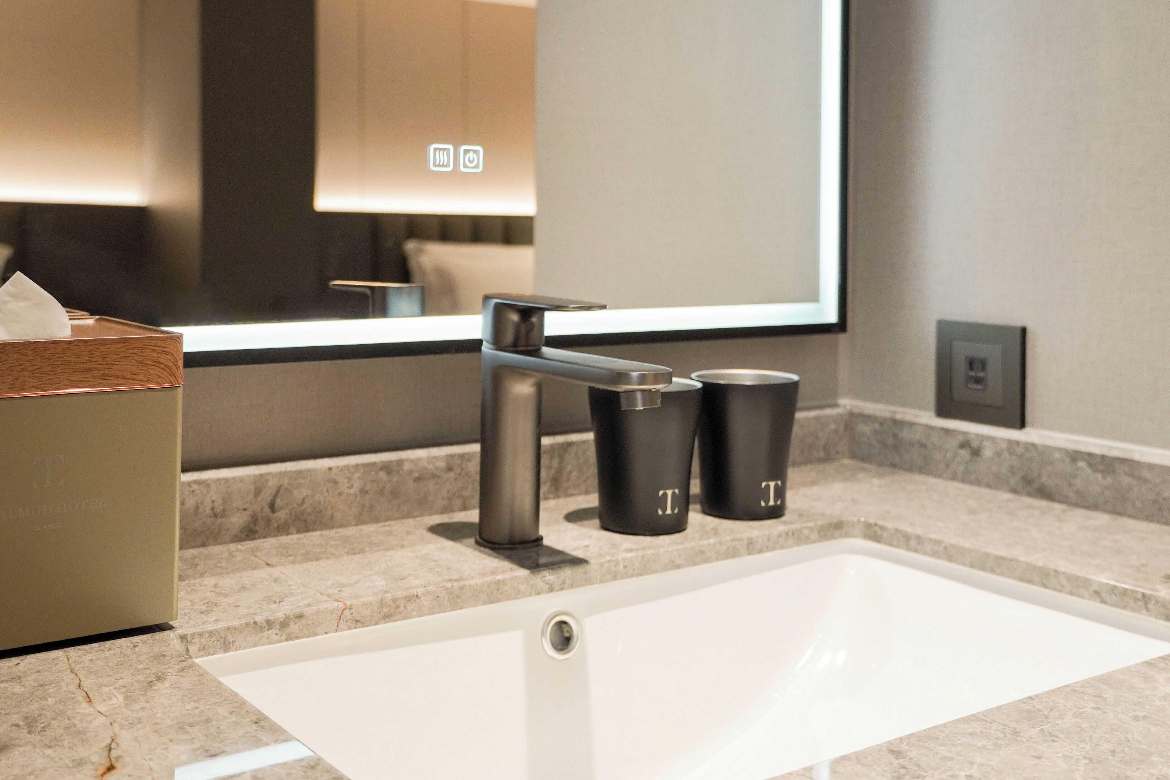 A modern bathroom with a white sink, a mirror, and two black containers on the countertop.