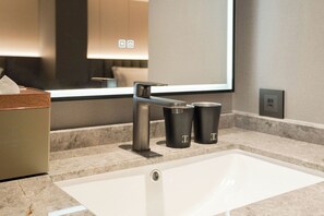 A modern bathroom with a white sink, a mirror, and two black containers on the countertop. - TALMUD HOTEL CLASSIC TAIWAN BOULEVARD (Taichung)