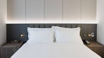 A hotel room with a large bed, two bedside tables, a wall-mounted phone, and a bedside lamp.