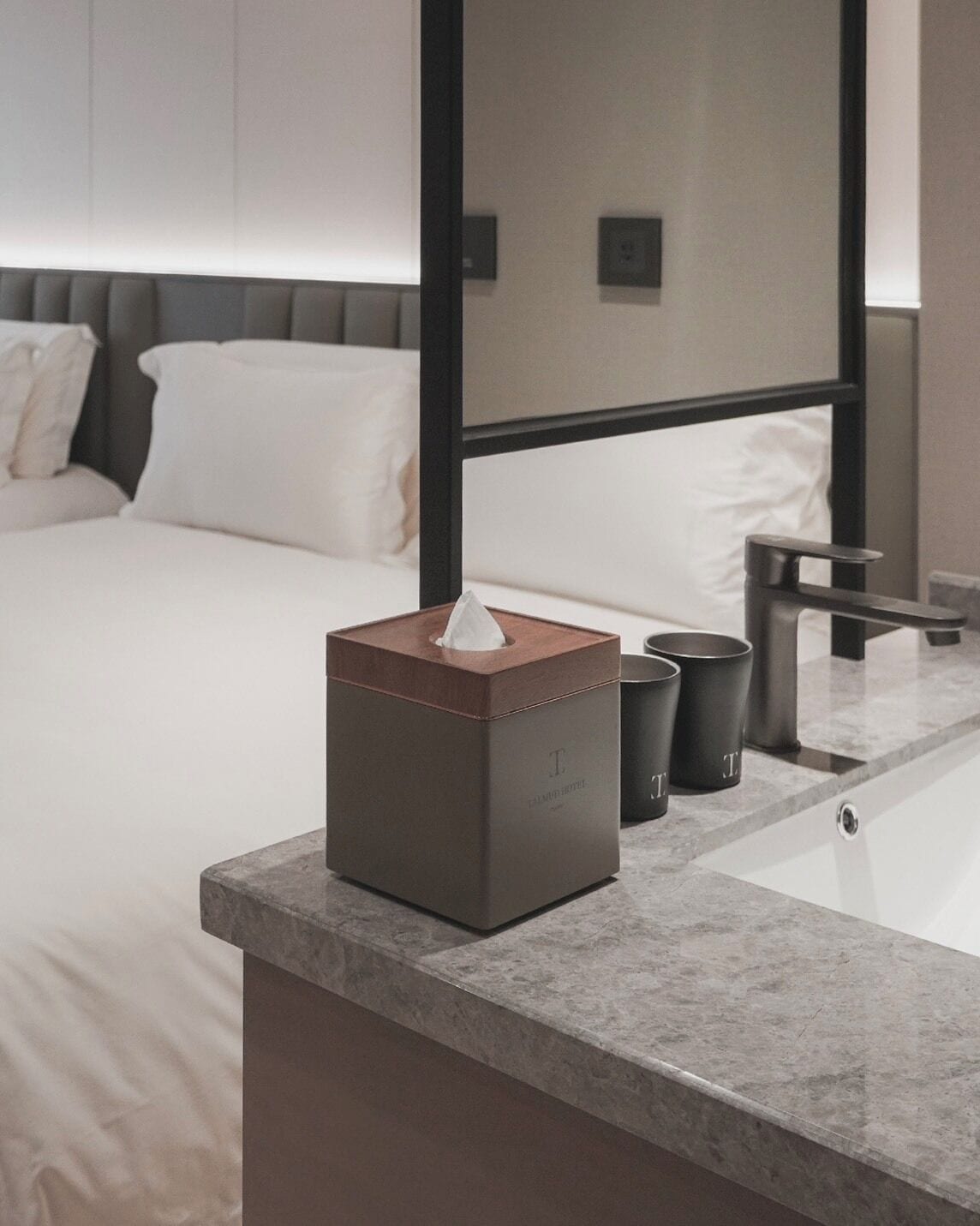 Une chambre d’hôtel avec un lit bien fait, une table de chevet avec une boîte de mouchoirs et une salle de bain moderne équipée d’une baignoire et d’un lavabo.